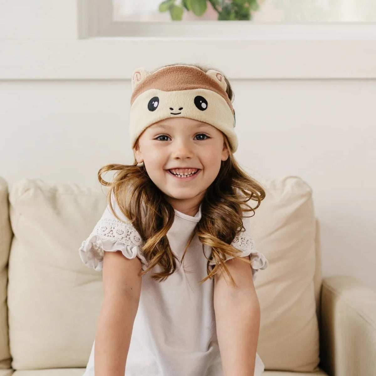 Child wearing a cute animal-themed headband sitting on a couch.